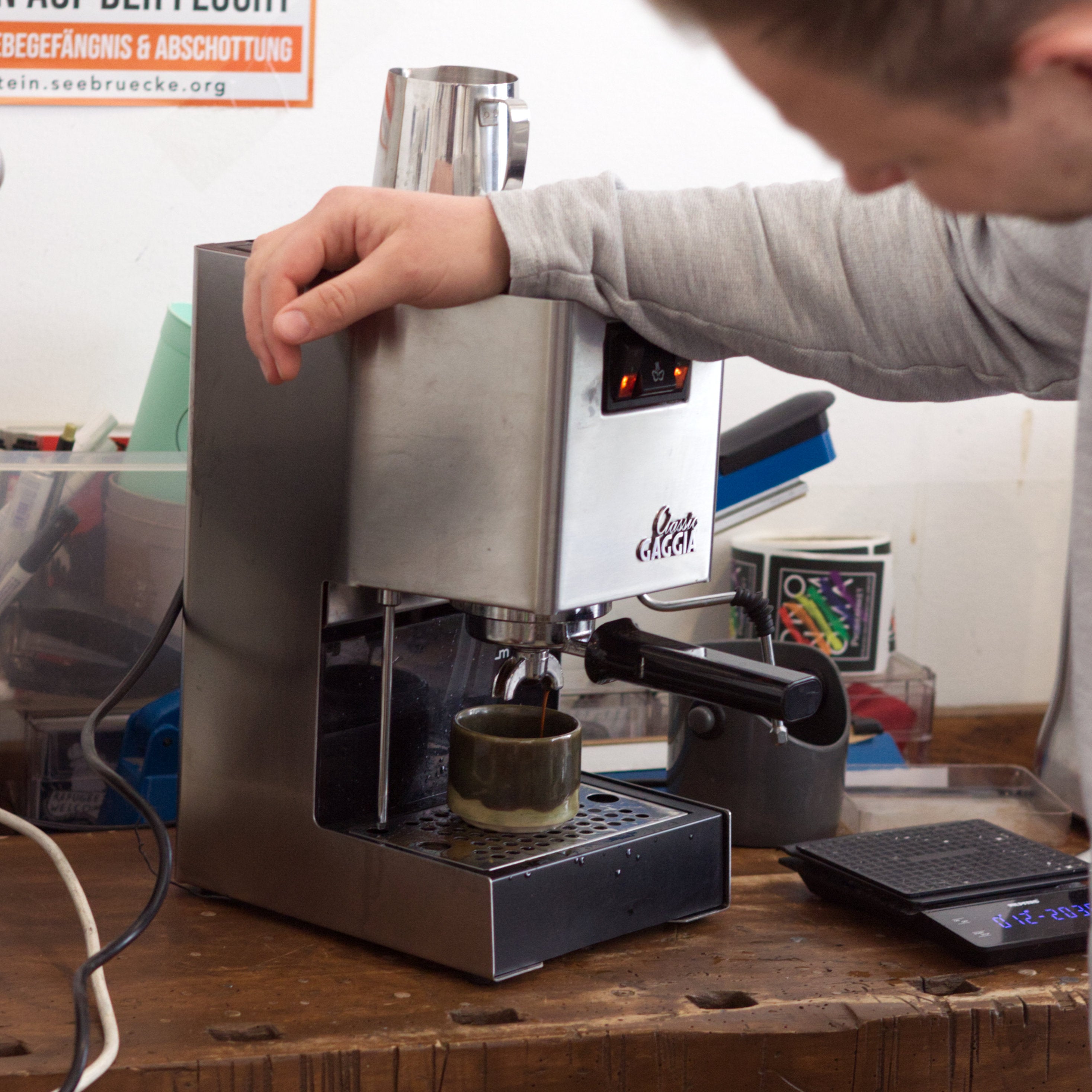 Ein Espresso läuft aus einer Gaggia-Siebträgermaschine. Ein Mensch lehnt darüber und begutachtet den Prozess.